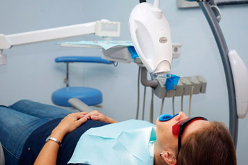 imagen de paciente recibiendo tratamiento láser en sus dientes recostada en silla de dentista.